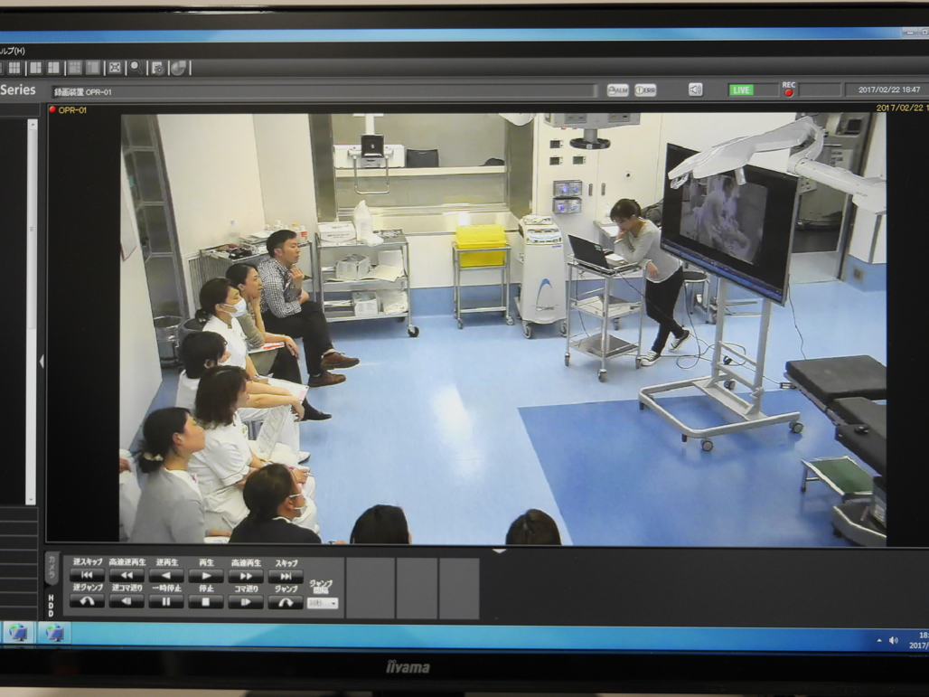 写真:実践の後に早速映像を見ながらデブリーフィングしている様子がモニターに映る