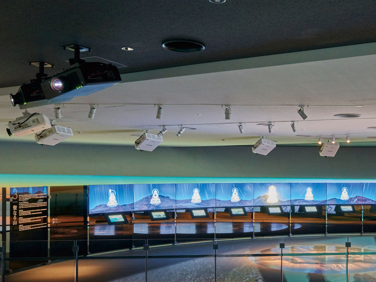 写真：展示ゾーンに所狭しと吊られたプロジェクター。天井材の色味に合わせて白色と黒色のキャビネットを使い分けることで、建築との調和が図られている