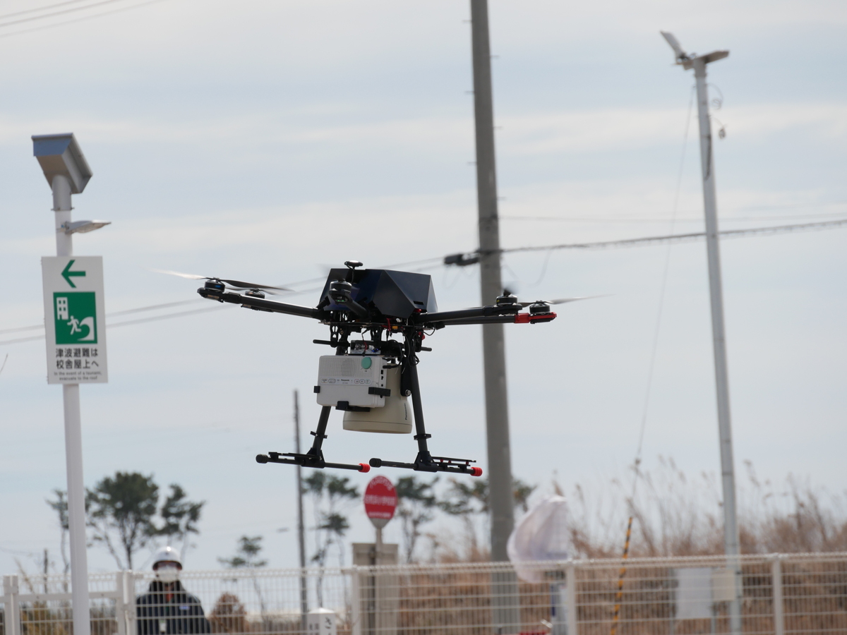 写真:防災⾏政無線受信機とスピーカーを搭載して⾶び⽴つドローン