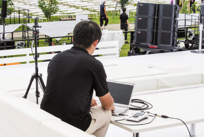 写真:パソコンで音響シミュレーションソフトPASDを設定している男性のうしろ姿。左手奥にスタンドに設置された測定用マイクが置かれている。