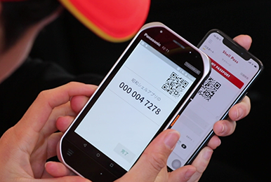 写真:スタッフがリーダー端末を使用してお客様のスマートフォンのQRコードを読み取り、チェックイン処理をする様子。