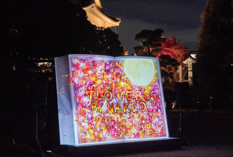 写真:東大手門にある大きな本のオブジェ。色鮮やかな花の背景の上に映し出される「FLOWERS BY NAKED」の文字。